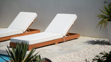 Twee witte ligbedden op een terras van Brasil White Flagstones, gecombineerd met witte kiezels, groene beplanting en een strakke grijze wand. een Ibiza achtige sfeer