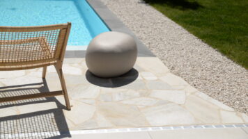 Detail van Brasil White Flagstones rondom een zwembad, gecombineerd met een donkere zwembadrand, witte kiezels en groen gazon. voor een Zuid-Europese sfeer in eigen achtertuin
