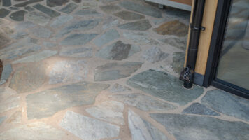 Detail van grijze Xanti Flagstones bij een glazen pui en regenpijp